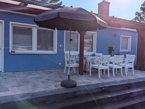 An outdoor patio with a table and chairs, a large umbrella, and a flower vase. - Double Vacation Bungalow in the Heart of the Schorfheide (Joachimsthal)