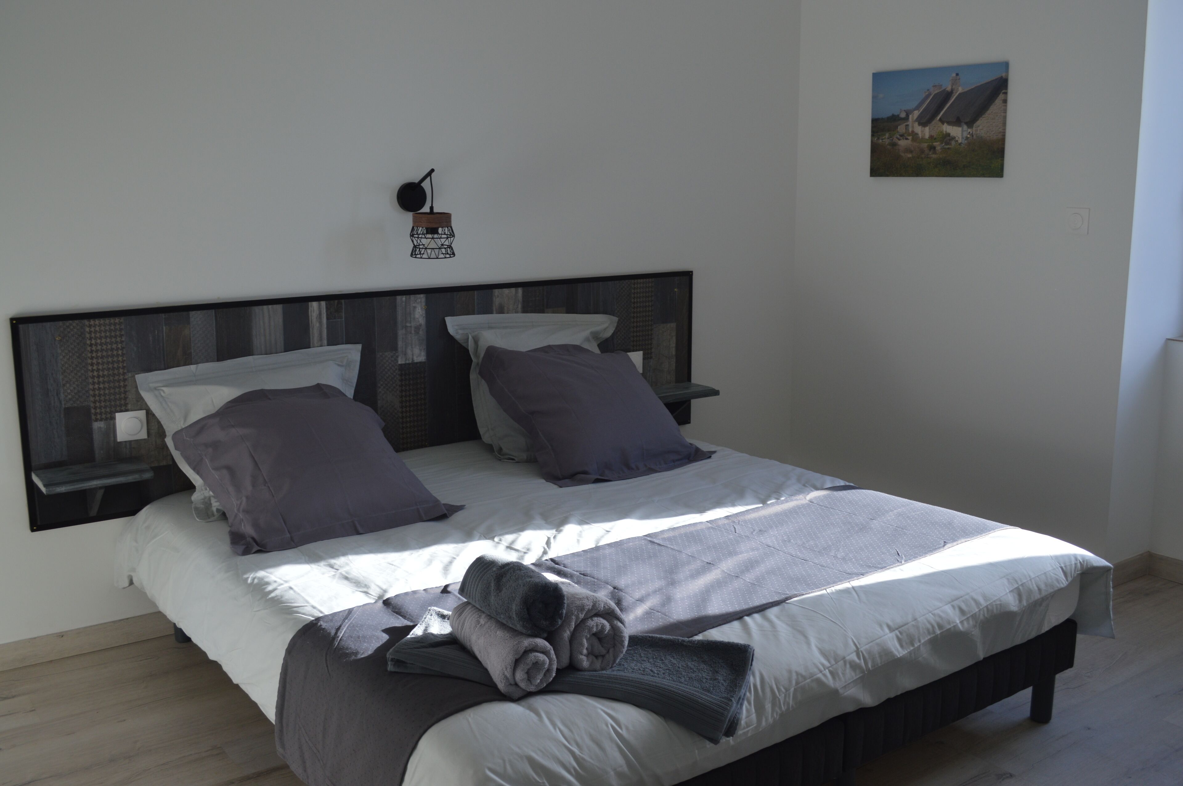 A bed with a headboard, two pillows, a blanket, and a rolled towel.