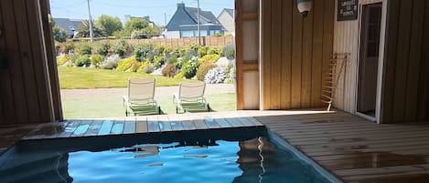 Une terrasse en bois avec une piscine, deux chaises longues et une vue sur un jardin et des maisons au loin.