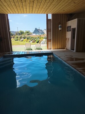 A wooden deck with a swimming pool, two lounge chairs, and a view of a garden and houses in the background.