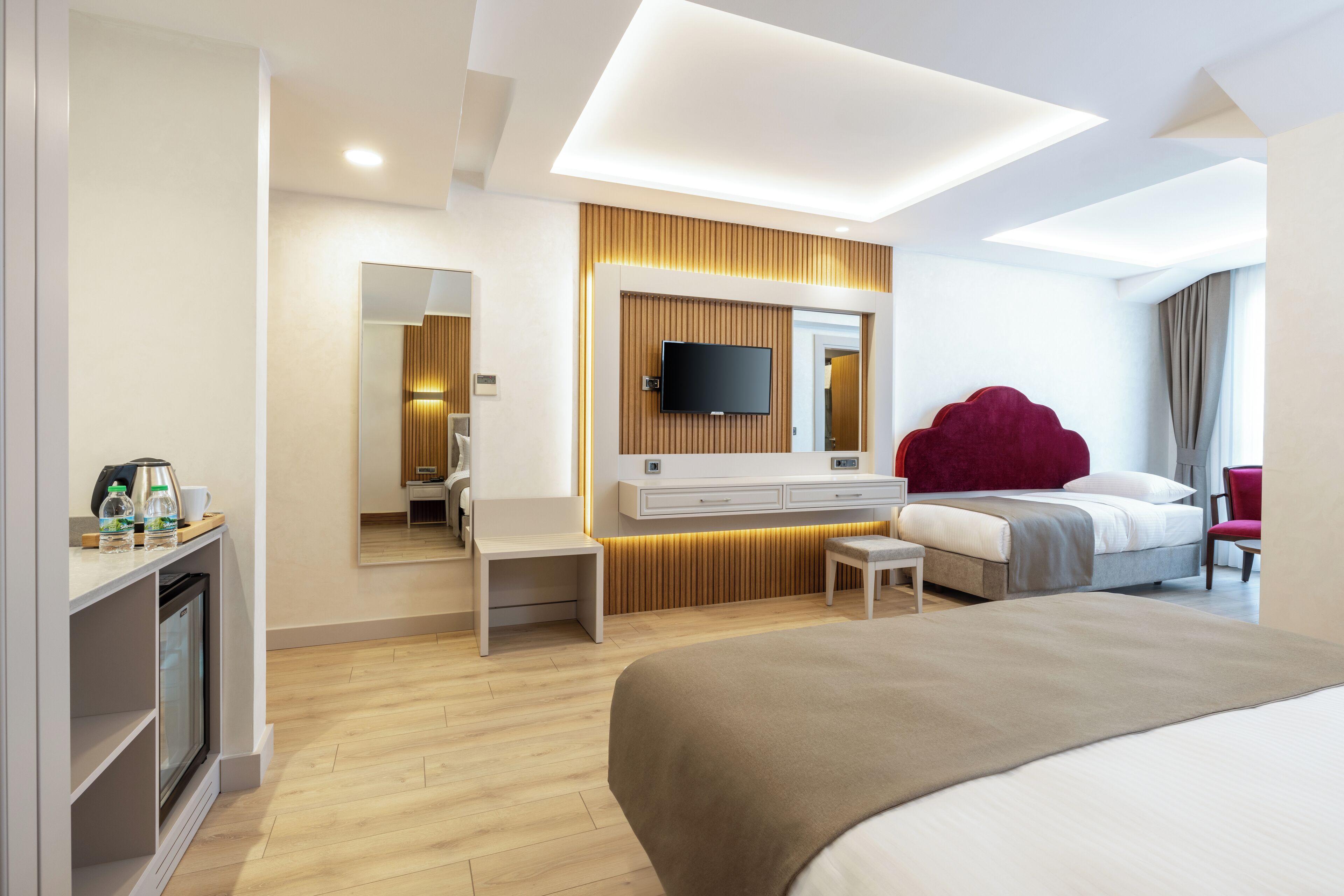A modern hotel room with a large bed, a TV mounted on a wooden panel wall, a small desk with a chair, and a mirror.