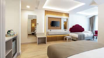 Een moderne hotelkamer met een groot bed, een televisie bevestigd aan een houten paneelwand, een klein bureau met stoel, en een spiegel.