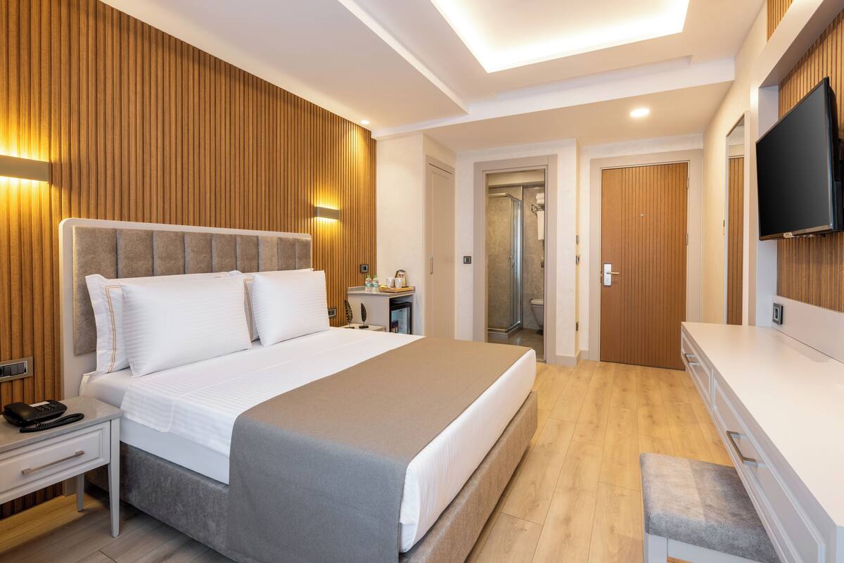 Moderni hotellihuone, jossa on suuri sänky, yöpöytä ja seinälle asennettu televisio.