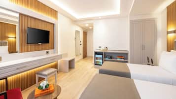 A modern hotel room with a flat-screen TV, a minibar, a seating area with a bench, and a large bed.