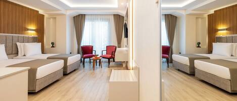 Una habitación de hotel moderna con dos camas, una zona de estar con sillones rojos y un espejo grande que refleja la habitación.