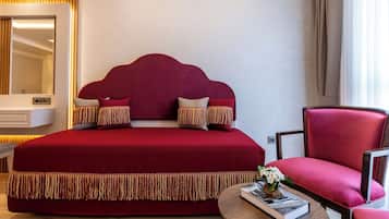 Una cama grande con cabecera roja, un sillón tapizado en rojo, una mesita de noche con un libro y un espejo con marco de madera.