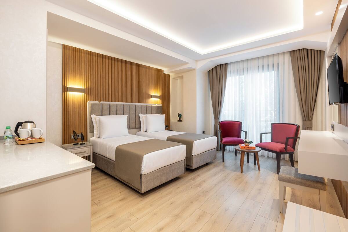 Hotellihuone, jossa on kaksi sänkyä, televisio, punainen tuoli ja pieni pöytä, jonka päällä on tarjotinalusta.