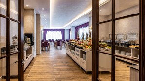 Et hotelmorgenmadsområde med buffet, trægulv og lilla gardiner.