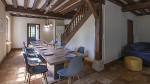 Un espace repas avec une longue table en bois, des chaises bleues et un escalier doté de rampes en bois.