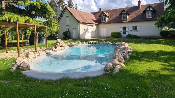 Une maison avec une piscine entourée de rochers, une pergola en bois et une pelouse bien entretenue.