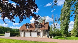 Una casa de estilo Tudor con una chimenea de ladrillo, puertas de garaje blancas y un césped bien cuidado.
