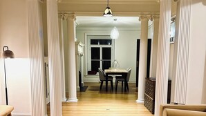 A living room with a wooden coffee table, a beige sofa, and a dining area with a table and chairs. - Historic Geneva Row House near Hobart William Smith Colleges and Linden Street. (Geneva)