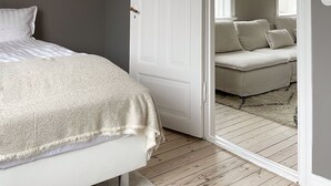 A bedroom with a bed, a white door, and a view into another room with a sofa. - Design apartments in Reykjavik (Reykjavik)