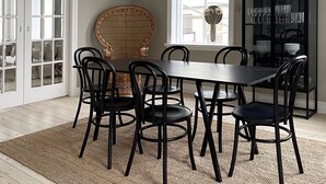 A dining area with a round table, black chairs, a wicker chair, a hanging light fixture, and a black cabinet with glassware. - Design apartments in Reykjavik (Reykjavik)