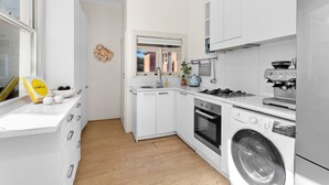 Uma cozinha moderna com armários brancos, forno embutido, máquina de lavar e janela com vista para o exterior.
