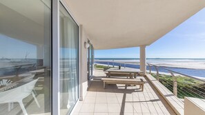 Varanda com vista para a praia, uma mesa e uma cadeira.