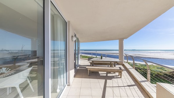A balcony with a view of the beach, a table, and a chair.
