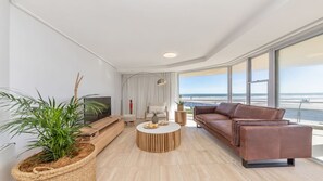 Uma sala de estar moderna com uma janela grande, um sofá de couro marrom, uma mesa de centro redonda e uma televisão.