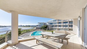 Ein Balkon mit Pool, Tisch und Blick auf Strand und Stadtlandschaft.