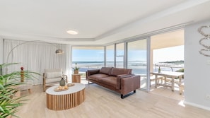 A modern living room with a leather sofa, a round coffee table, and a view of the sea through large windows.