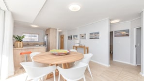 A modern kitchen with white cabinets, a wooden island, and a dining area with a round wooden table and white chairs.