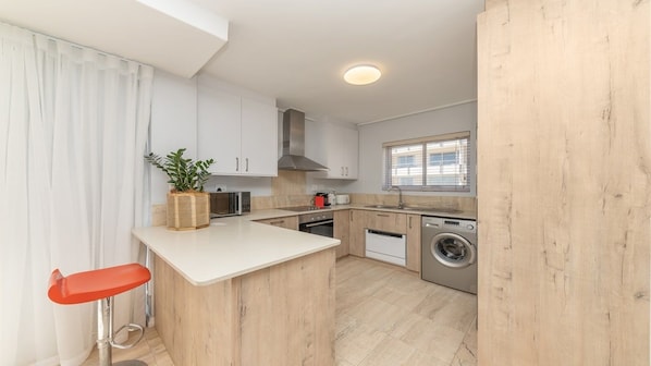 A modern kitchen with white cabinets, a central island, a washing machine, and a window with blinds.