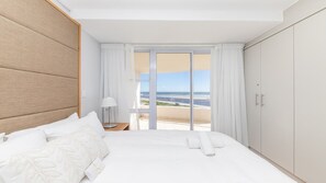 Ein Hotelzimmer mit Bett, Nachttisch, Lampe, Meerblick und Kleiderschrank.