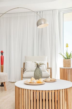 A modern living room with a round wooden coffee table, a white sofa, and a large window with white curtains.
