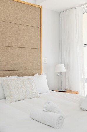 Quarto de hotel com cama, mesa de cabeceira, abajur e janela com cortinas.