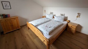 Ett sovrum med en säng i trä, två sängbord, en byrå i trä och en väggmonterad lampa.