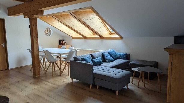Ett rum i loftstil med en matplats, en grå hörnsoffa och ett träskåp.
