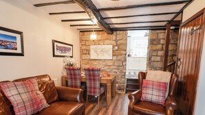A cozy living room with a brown leather sofa and armchair, plaid cushions, a wooden coffee table, and a stone wall. - Midships Cottage (Whitby)