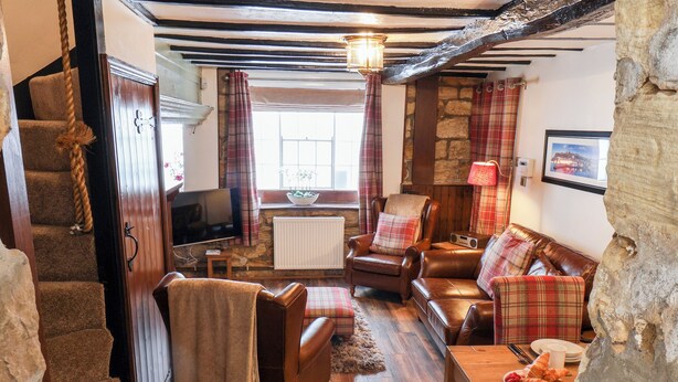 A cozy living room with a fireplace, a television, and a dining area with a table set for breakfast. - Midships Cottage (Whitby)