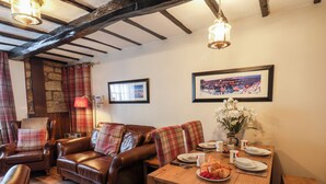 A cozy living room with a brown leather sofa, plaid cushions, a wooden dining table set with plates, cups, and a vase of flowers. - Midships Cottage (Whitby)