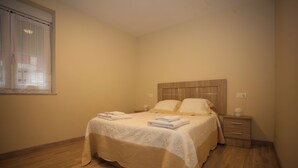 A bedroom with a bed, a nightstand, and a window with curtains.