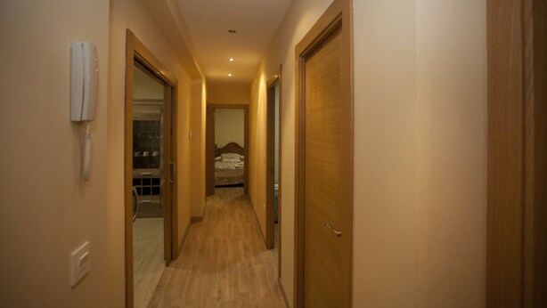A narrow hallway with wooden doors and a telephone on the left wall.