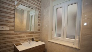 A bathroom with a marble vanity, a mirror, and a window with frosted glass.