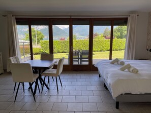 A hotel room with a bed, a dining table with chairs, and a large sliding glass door leading to a garden.