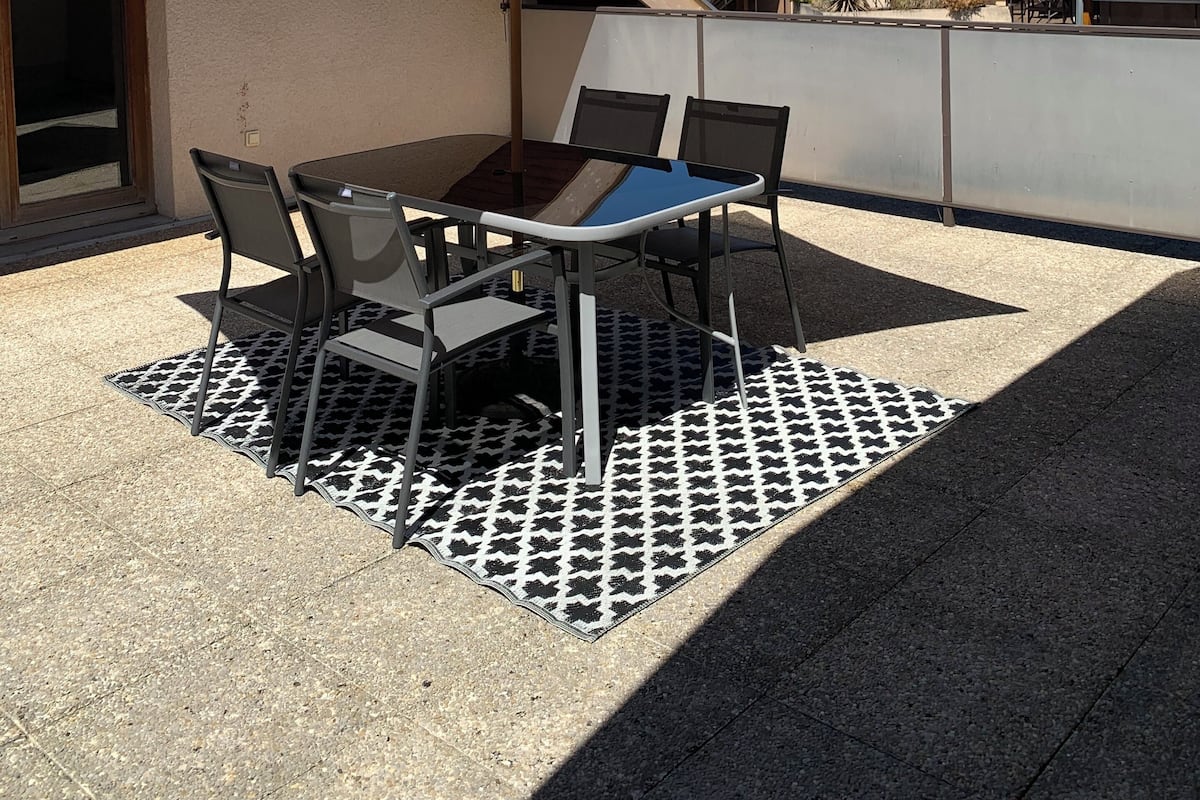 An outdoor patio with a table and chairs, a large umbrella, and a view of mountains in the background.