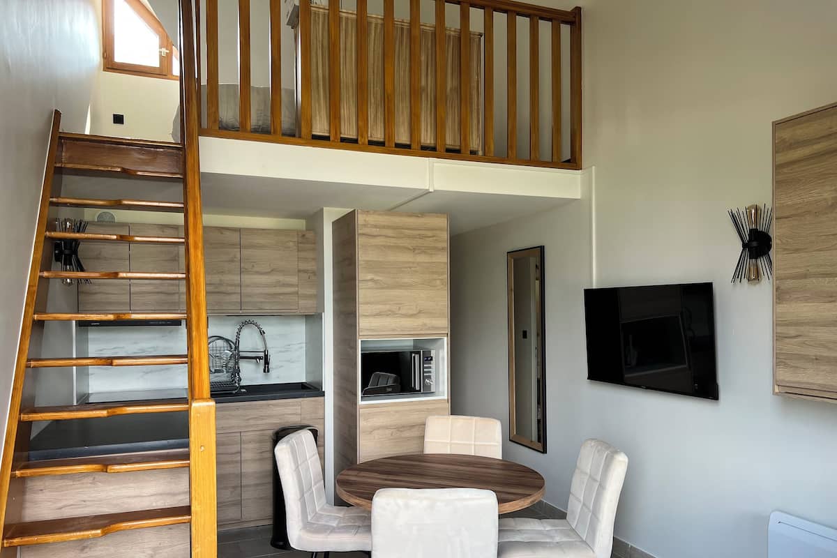 A modern kitchen with wooden cabinets, a built-in microwave, and a dining area with a round table and four chairs.