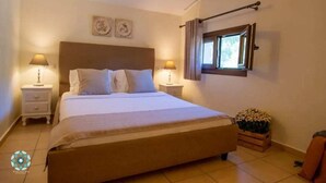 Ein Schlafzimmer mit einem großen Bett, zwei Nachttischen mit Lampen, einem Fenster mit Vorhängen und einer kleinen Holzkiste mit Blumen.