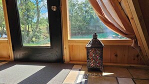 Interior de madera con una puerta negra, un pequeño farol decorativo y vistas a la vegetación exterior.