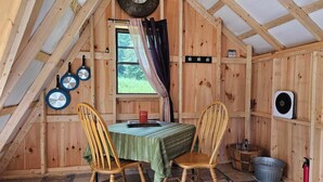 Una cabaña acogedora de madera con una mesa de comedor, dos sillas, un reloj y una ventana con cortinas.
