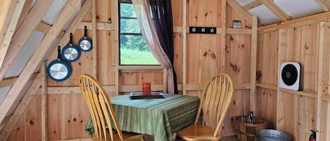 A cozy wooden cabin with a dining table, two chairs, a clock, and a window with curtains.