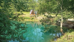 Una cabaña rústica junto a un lago tranquilo rodeada de árboles frondosos.