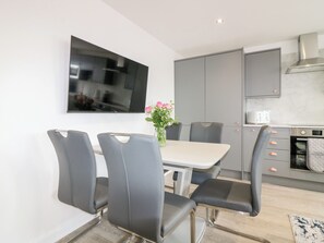 A modern kitchen with grey cabinets, a built-in oven, and a dining area with a table and chairs. - 111a Main Street (Banff)