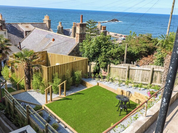 A backyard with a green lawn, a wooden fence, and a view of the sea. - 111a Main Street (Banff)