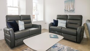 Un salon moderne avec deux canapés en cuir, une table basse blanche et un tableau représentant des voiliers accroché au mur.