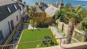 Une cour avec une petite pelouse, une clôture en bois et une vue sur la mer.
