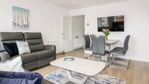 Un salon moderne avec un canapé gris, une table basse et un coin repas comprenant une table et des chaises.